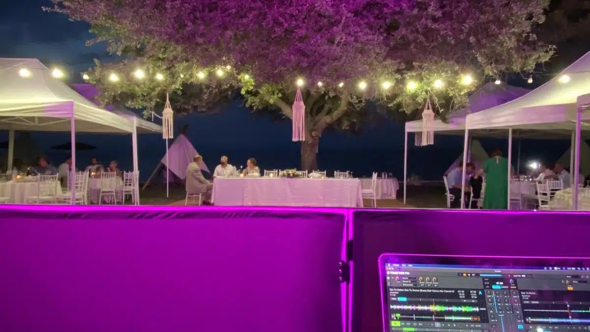 Κονσόλα DJ σε δεξίωση γάμου δίπλα στη θάλασσα με μωβ φωτισμό ατμόσφαιρας