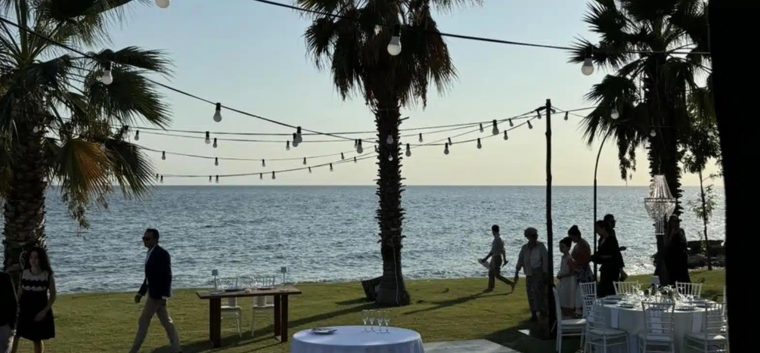 Εξωτερικός χώρος εκδήλωσης δίπλα στη θάλασσα με φωτάκια και τραπέζια το απόγευμα